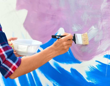 female-artist-working-on-abstract-acrylic-painting-hand-holding-paint-brush-large-canvas-outdoor.jpg