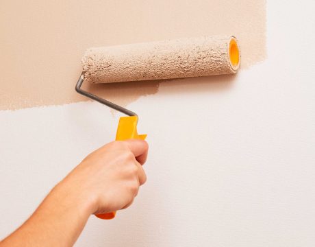 Repair in the house. A man paints the walls with a roller in beige color